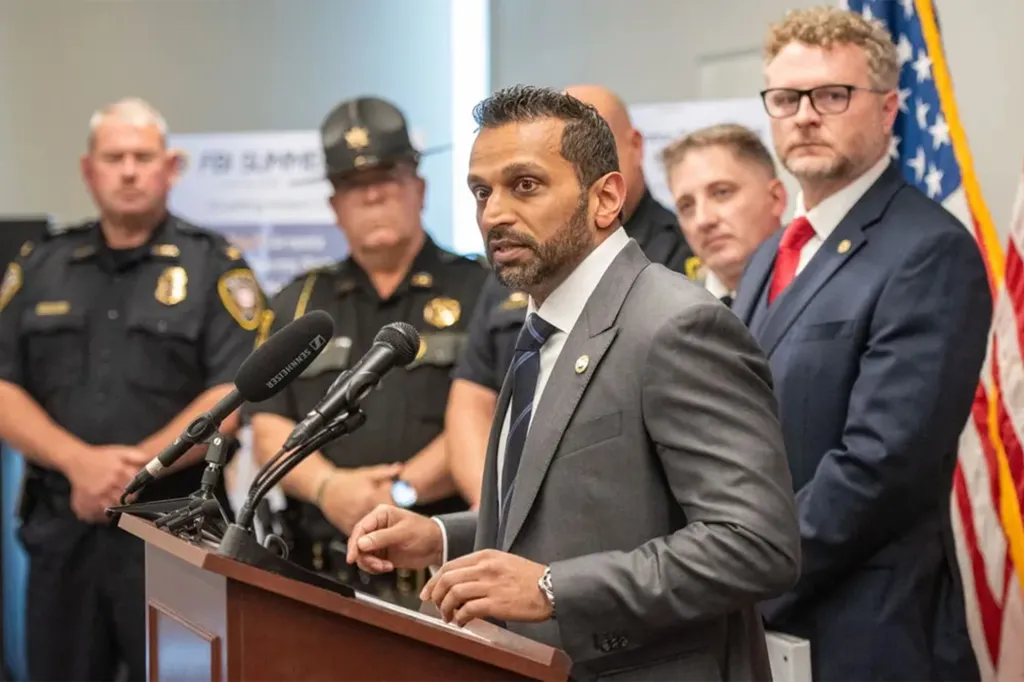 A man in a suit speaks at a podium with microphones, flanked by law enforcement officers, announcing the results of Operation Turf War.