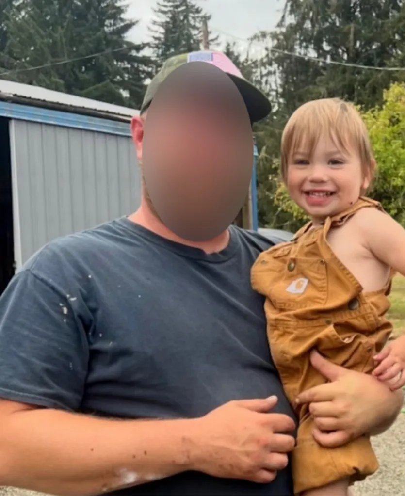A man holding a smiling toddler in brown overalls.