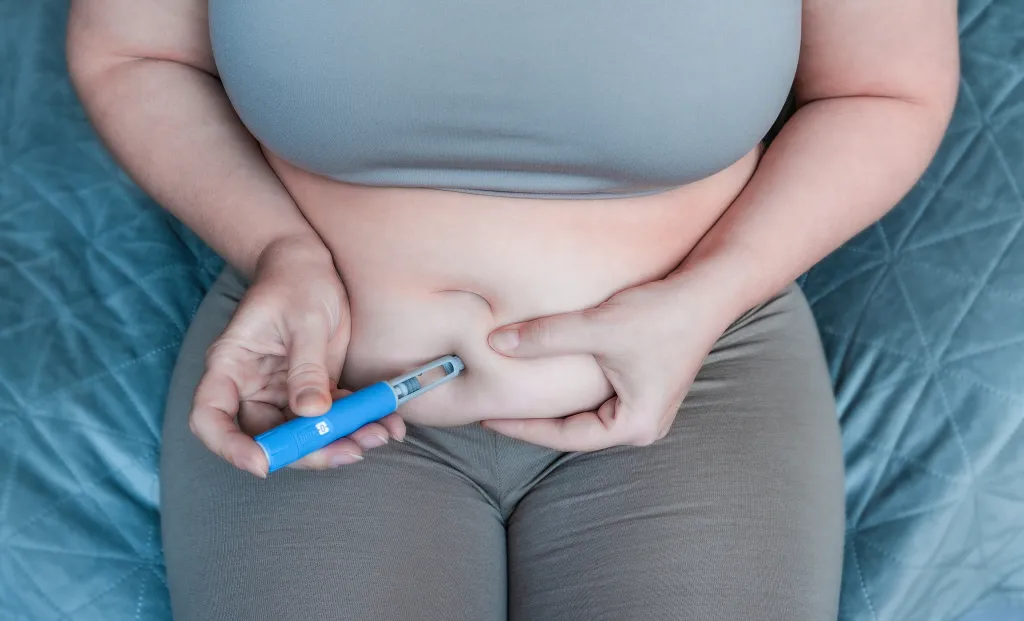 Woman injecting GLP-1 agonist into her abdomen for weight loss.