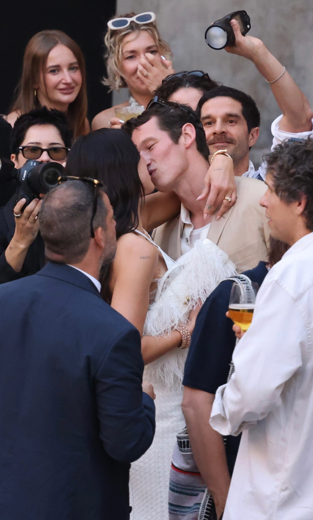 Dua Lipa and Callum Turner kissing with people around them.