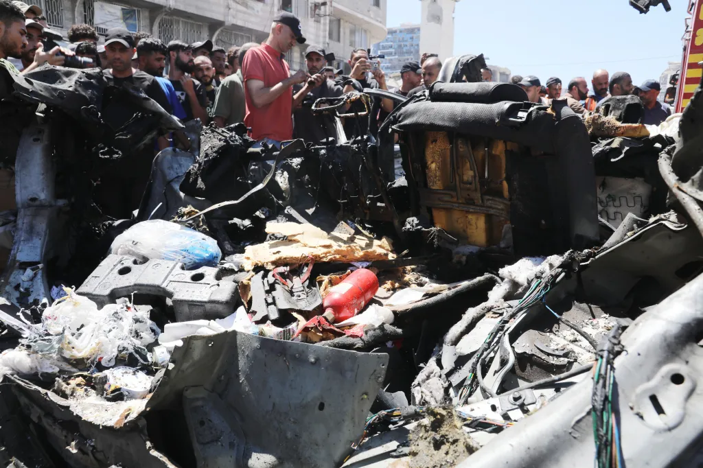 Destroyed vehicle in Gaza City after an Israeli airstrike, with onlookers in the background.