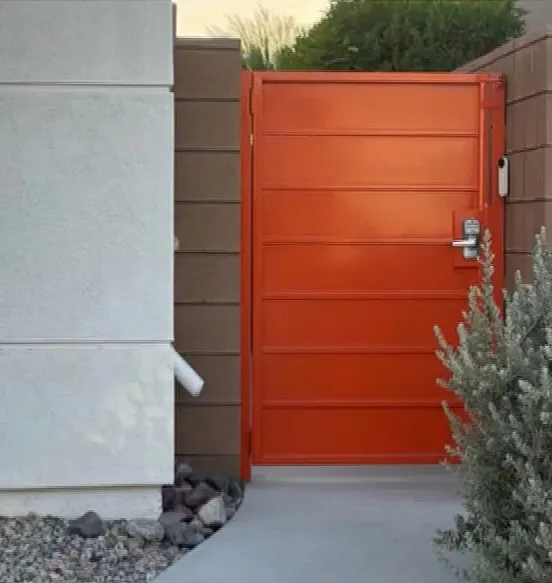 A bright orange gate with horizontal panels and a digital lock, next to a white stucco wall.