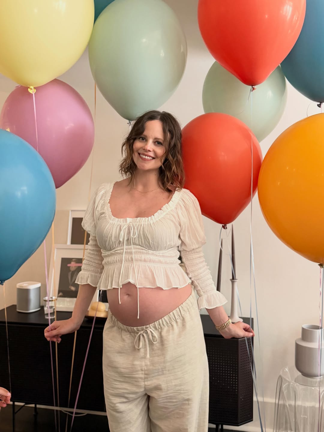 Parenthood's Sarah Ramos, pregnant and smiling, stands among colorful balloons.