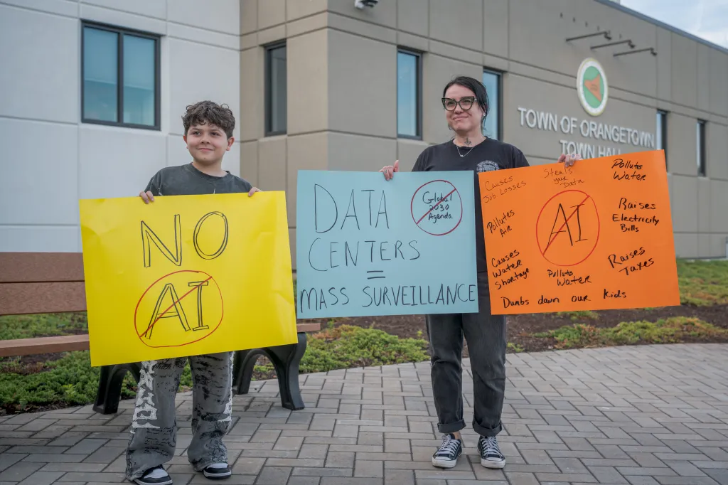 Protesters hold signs against AI and data centers, advocating for environmental protection and local concerns.