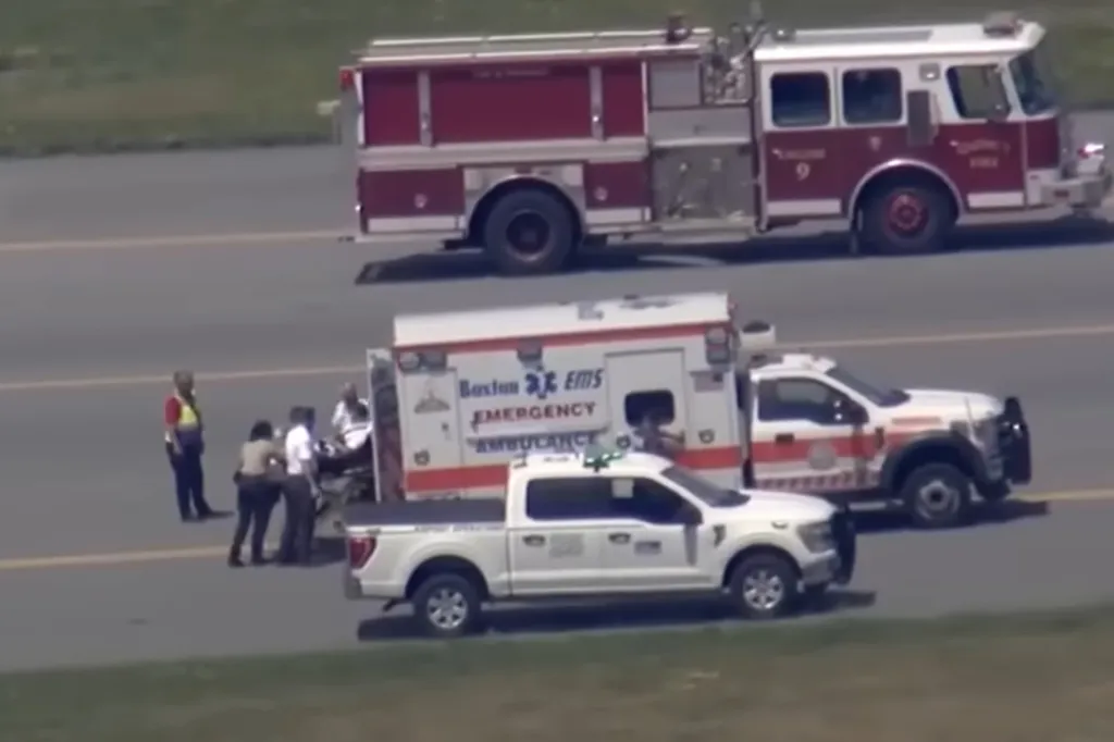 Emergency services personnel assist a person on a stretcher on an airport tarmac, with an ambulance, fire truck, and pickup truck nearby.