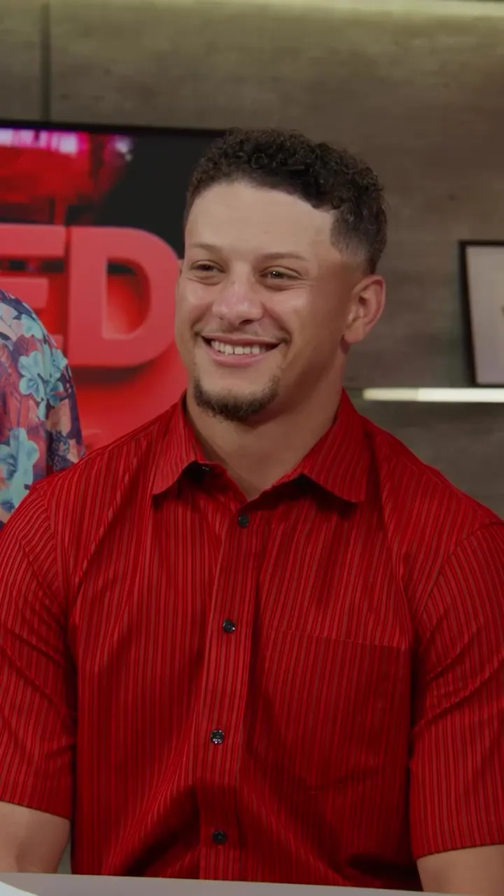 Patrick Mahomes smiling while wearing a red pinstriped button-up shirt.