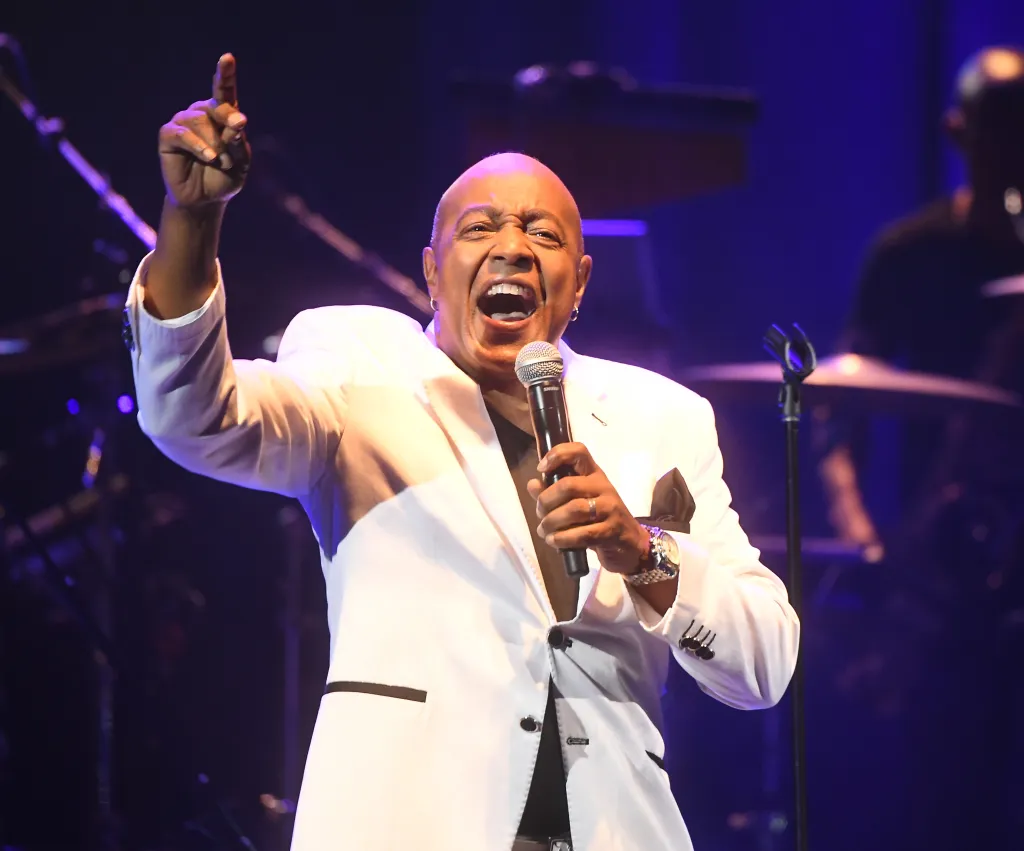 Peabo Bryson singing into a microphone on stage, with his left hand raised and pointing.