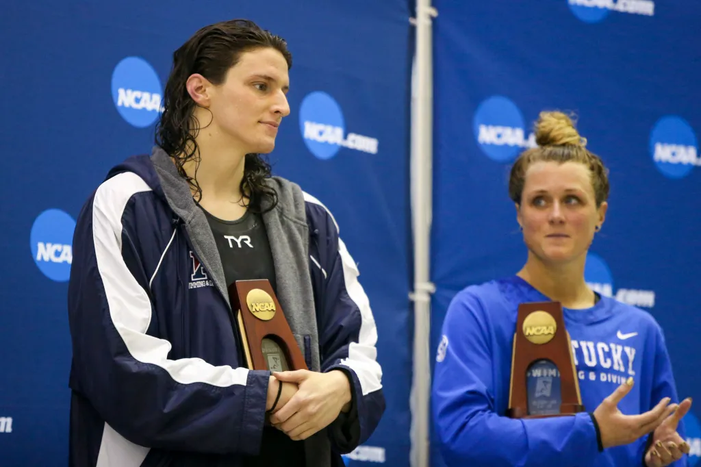 Lia Thomas holding a trophy after finishing fifth, with Riley Gaines looking on.