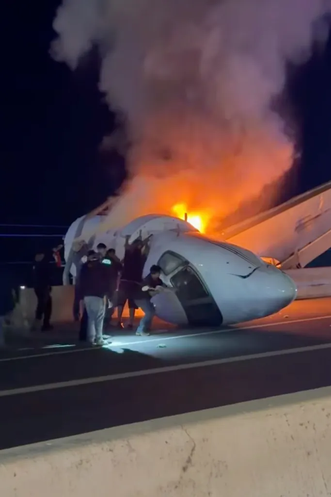 People attempting to pull passengers from a plane on a highway after it crashed and caught fire.