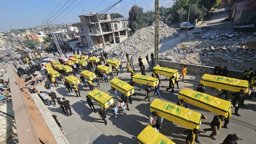 A funeral procession in Lebanon with many yellow coffins draped with Hezbollah flags.