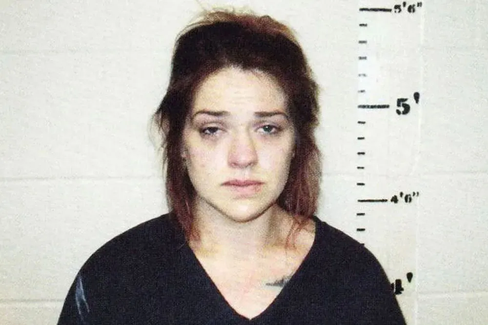 Booking photo of Taylor Rene Parker, a woman with light brown hair pulled back, wearing a black shirt, against a white height chart background.