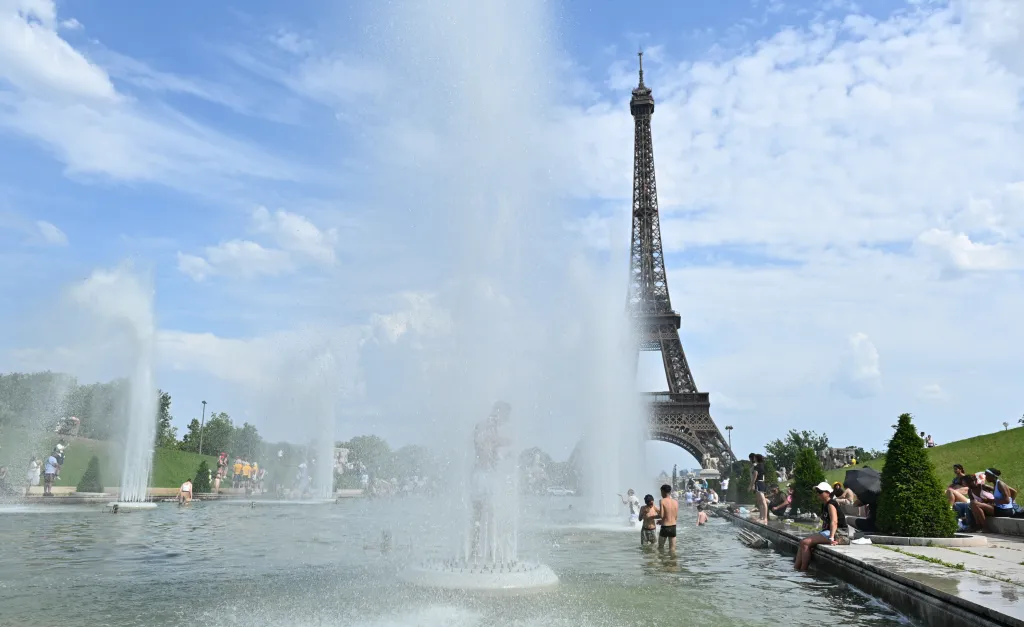 People cooling off in the Trocadero Gardens fountains in Paris during a heatwave, with the Eiffel Tower in the background.