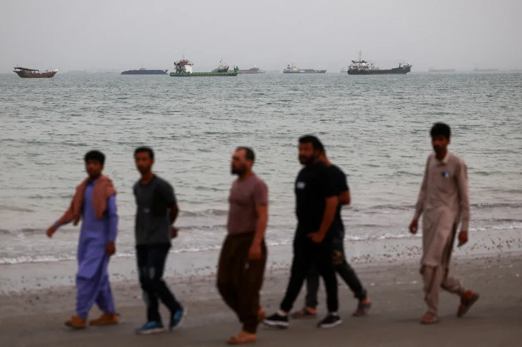 People walk on the beach near vessels in the Strait of Hormuz.