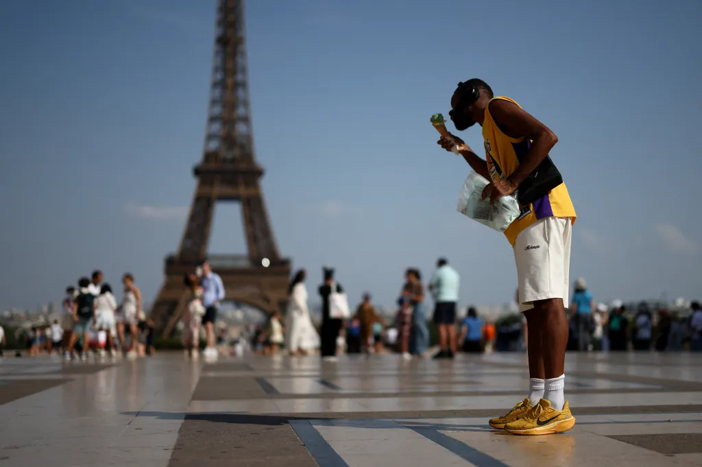 A person eats ice cream in front of the Eiffel Tower during a heatwave in Paris.