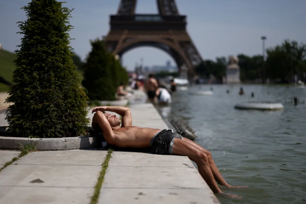 A person sunbathing next to the Trocadero Fountains by the Eiffel Tower with their feet in the water during a heatwave in Paris.