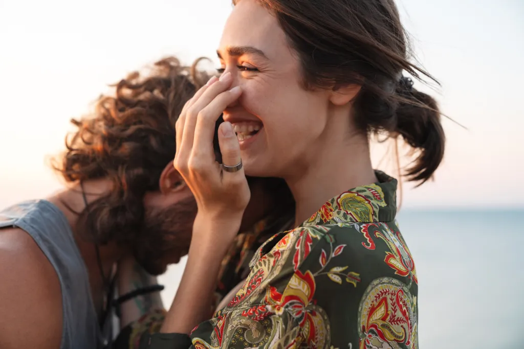 Closeup of a smiling woman in a patterned shirt with a man's head on her shoulder.