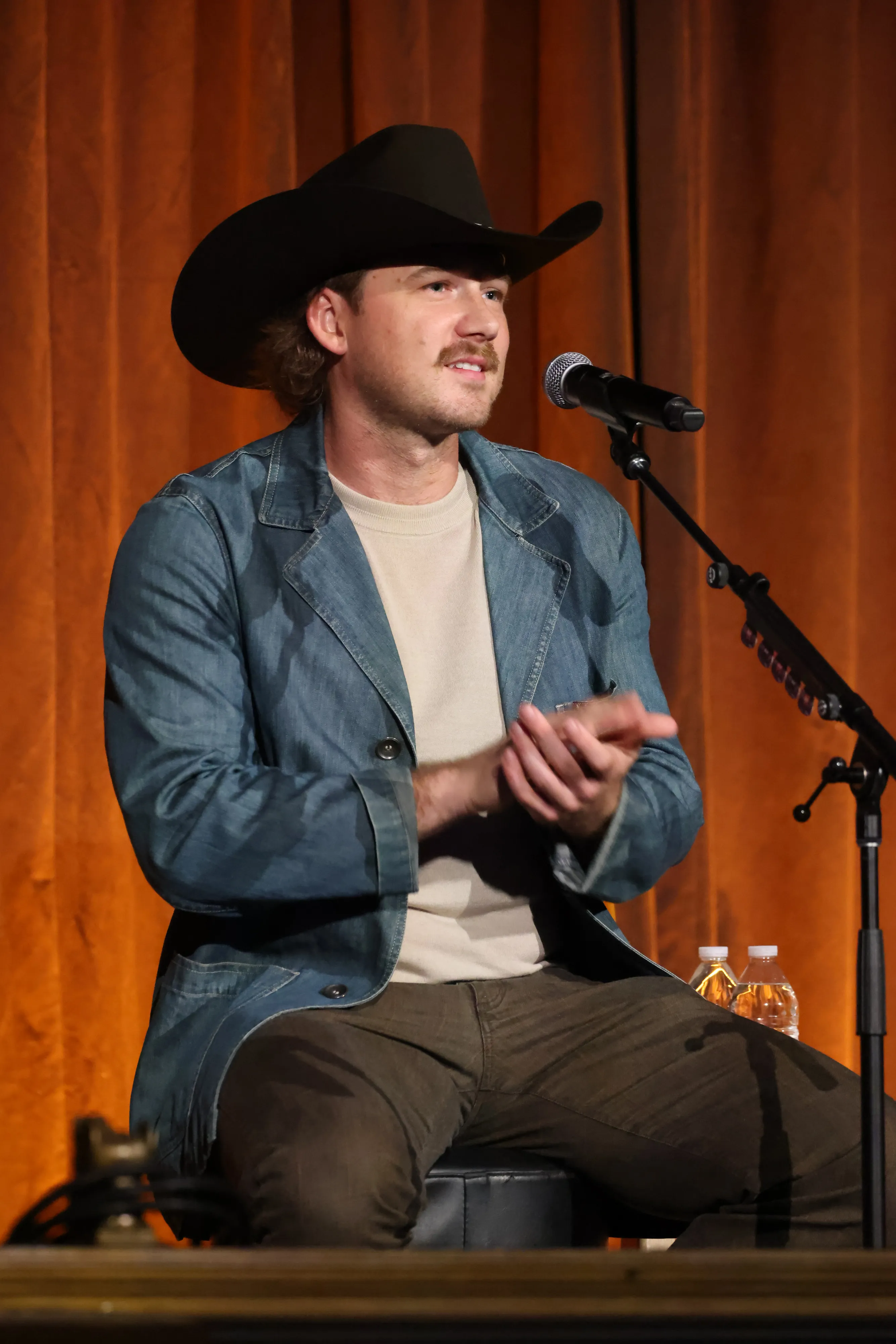 Morgan Wallen on stage in a cowboy hat and denim jacket, clapping.