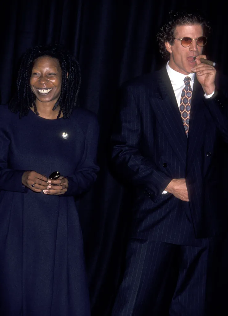 Whoopi Goldberg smiling next to Ted Danson, who is smoking a cigar.
