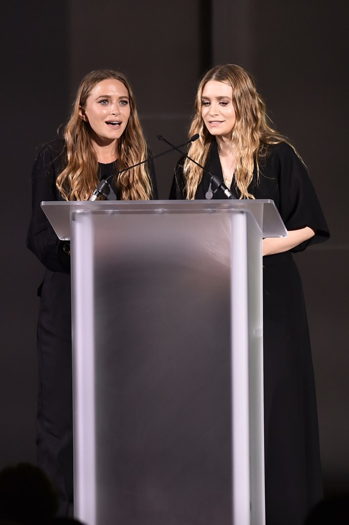 Mary-Kate Olsen and Ashley Olsen speaking at a podium.