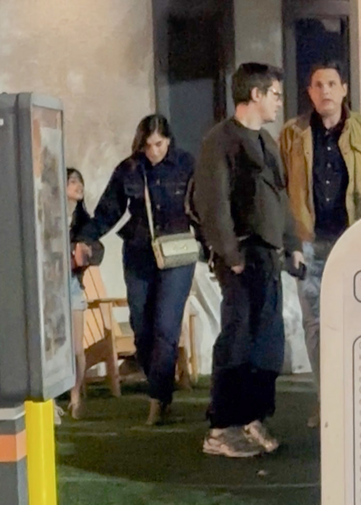 John Mayer and Kat Stickler walking at night with another man behind them.