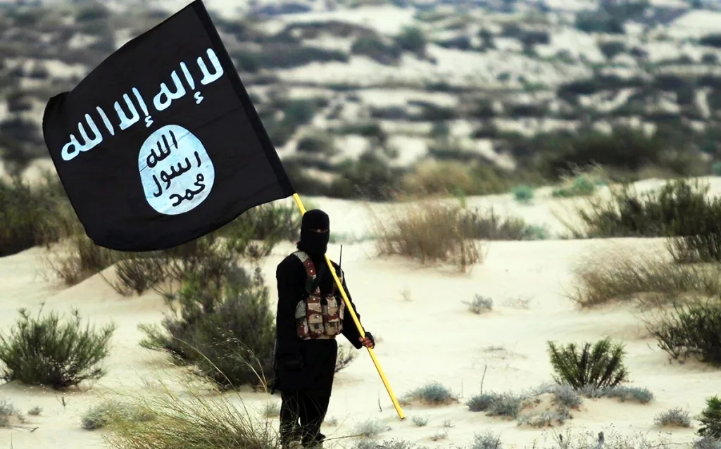 An Islamic State soldier in a desert holds an ISIL banner.