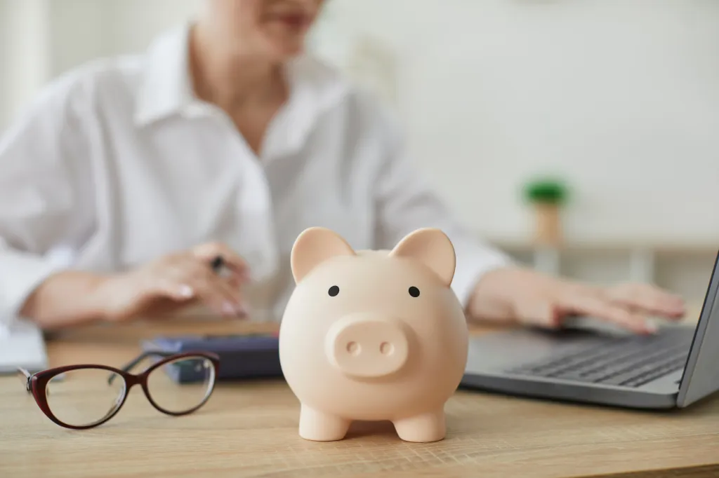 A piggy bank on a desk, with a financial advisor calculating a budget in the background.