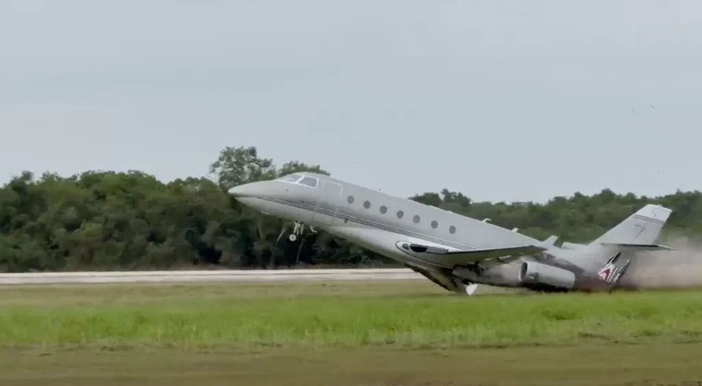 A Gulfstream jet crashes on the runway, with its front end pointing upwards and the tail end impacting the ground, kicking up smoke.