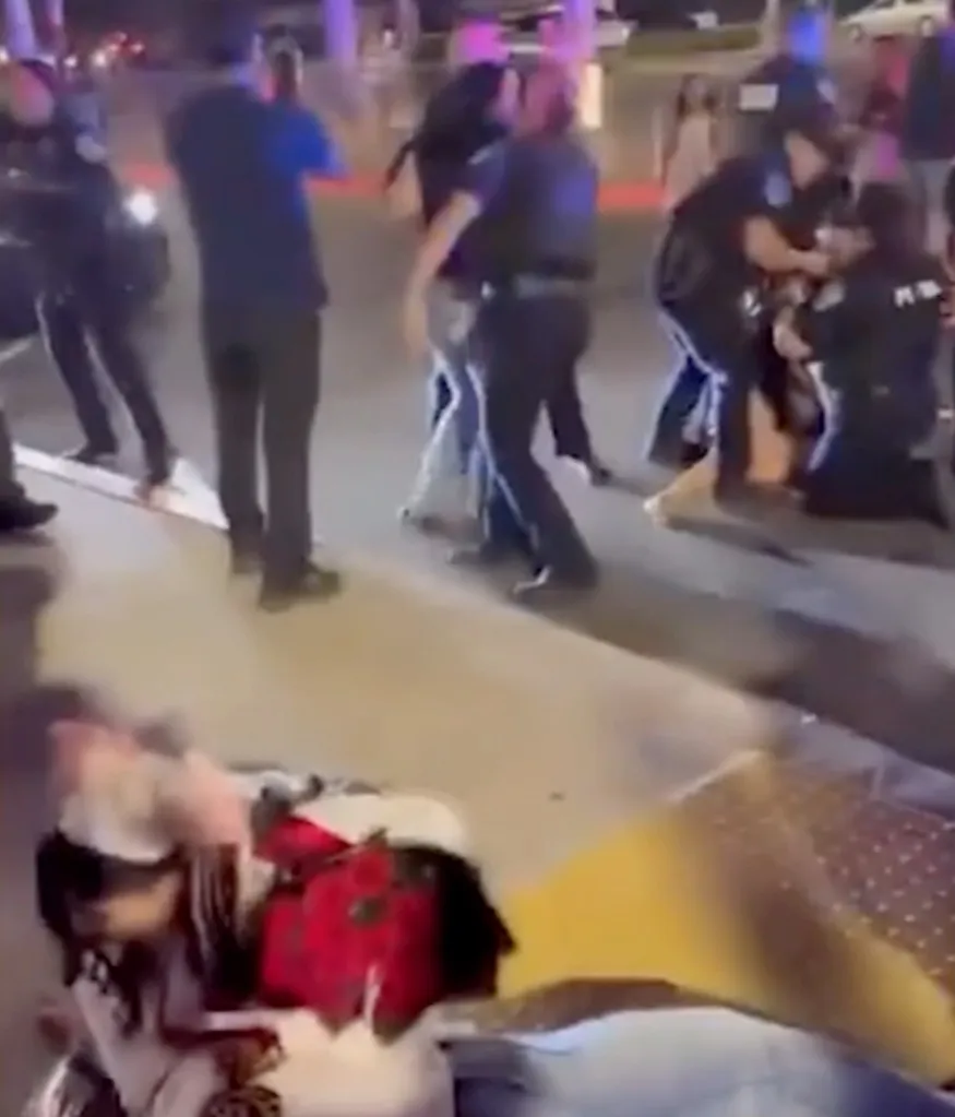 Police officers engaging with several people, one officer on the right kneels over someone on the ground.