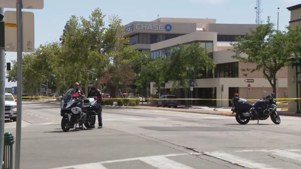 Police officers and motorcycles on a street blocked with yellow tape, with a Chase Bank building in the background.