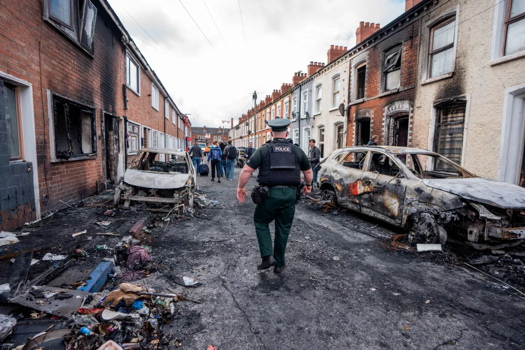 Police officer inspecting burnt out cars and buildings in Templemore, Belfast, following a protest.