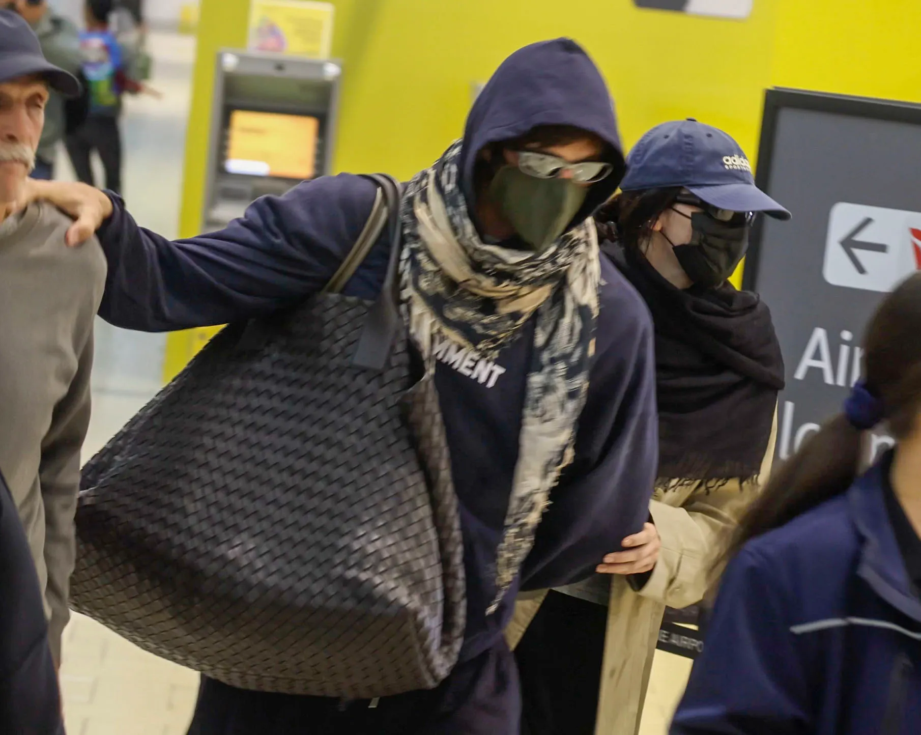 Jacob Elordi and Kendall Jenner in hoodies, face coverings, and sunglasses at Brisbane Airport.