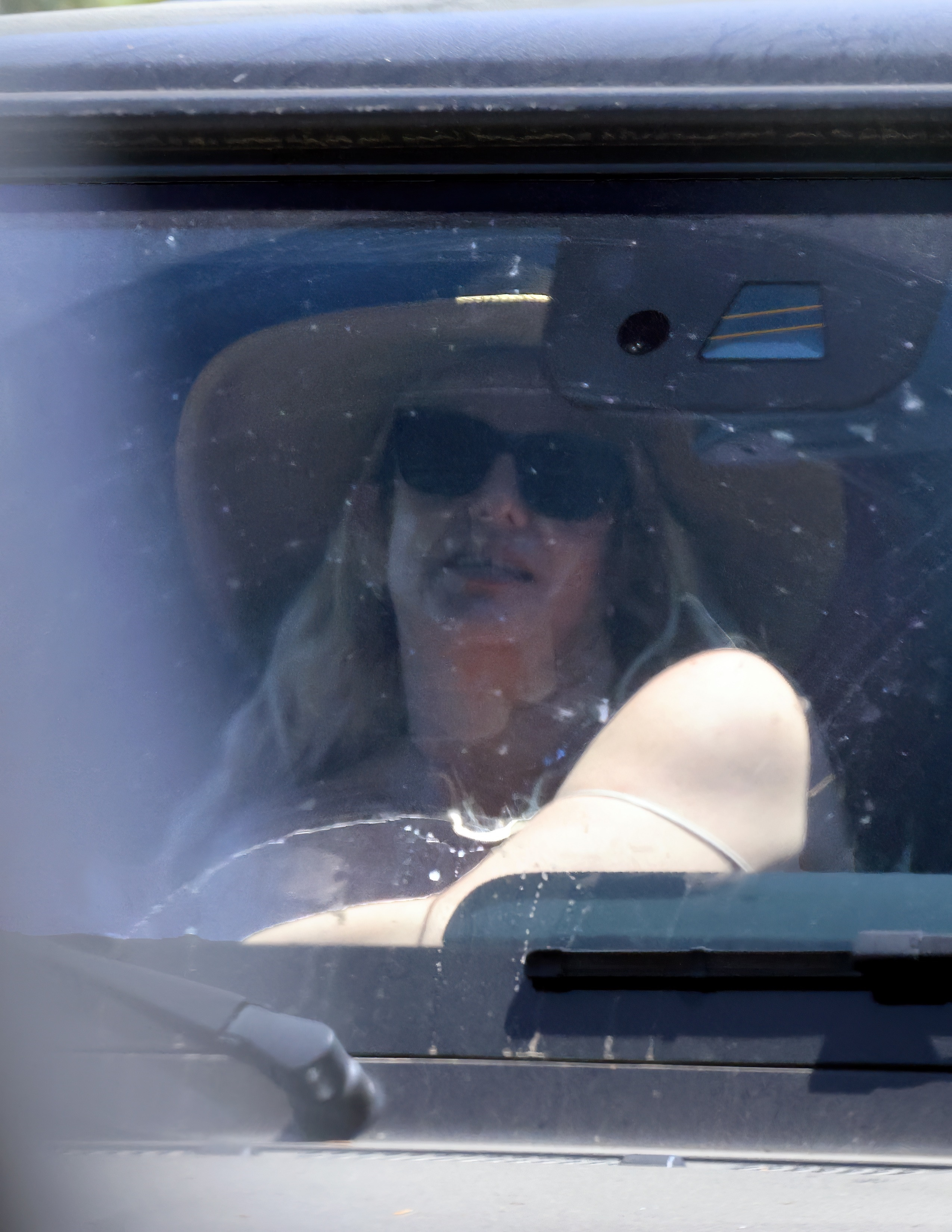 Britney Spears in the passenger seat of a car, wearing a wide-brim hat and sunglasses.