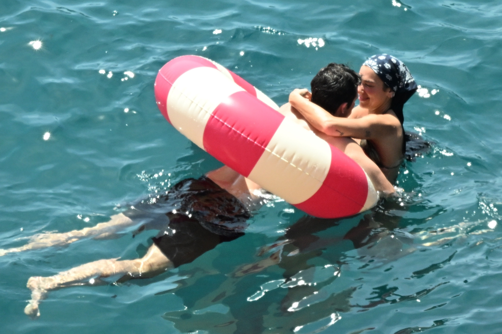 Dua Lipa and Callum Turner embracing in the water while resting on a red and white inflatable tube.