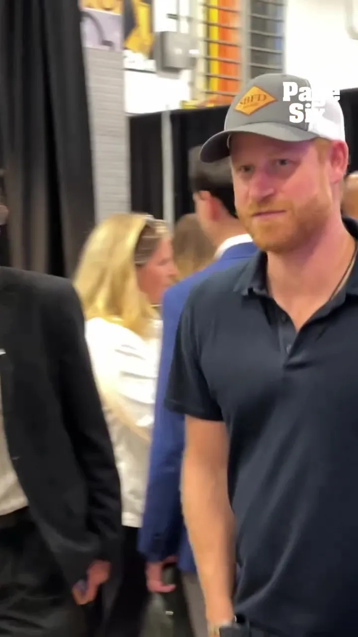 Prince Harry wearing a gray and white baseball cap and a navy polo shirt.