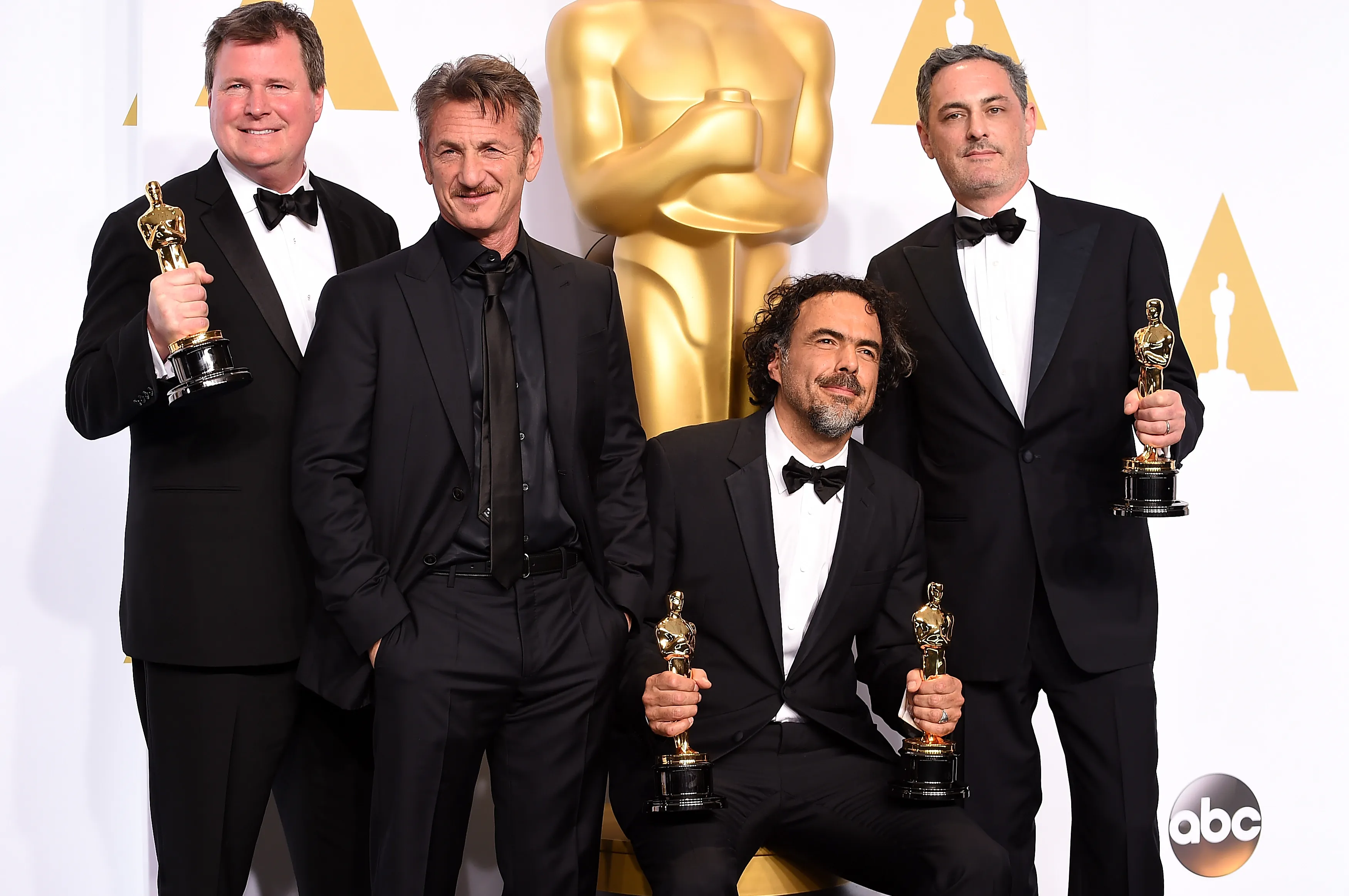 Four men in suits pose with Oscar trophies.