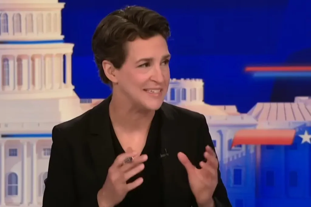 Rachel Maddow speaking, gesturing with her hands, in front of a blue background with white architectural elements.