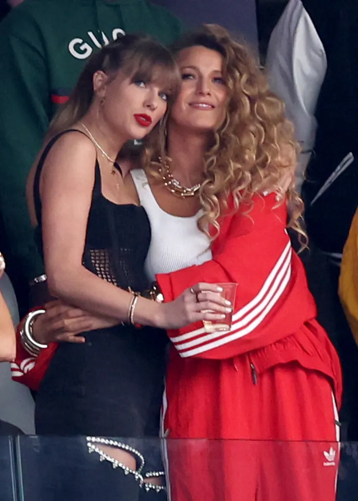 Taylor Swift in a black top with Blake Lively in a red Adidas jacket.