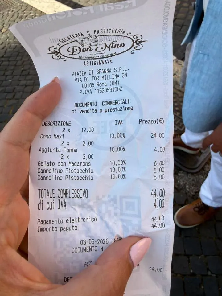 A hand holding a gelateria receipt showing a €44 charge for two maxi cones, whipped cream, gelato with macarons, and two pistachio cannoli.
