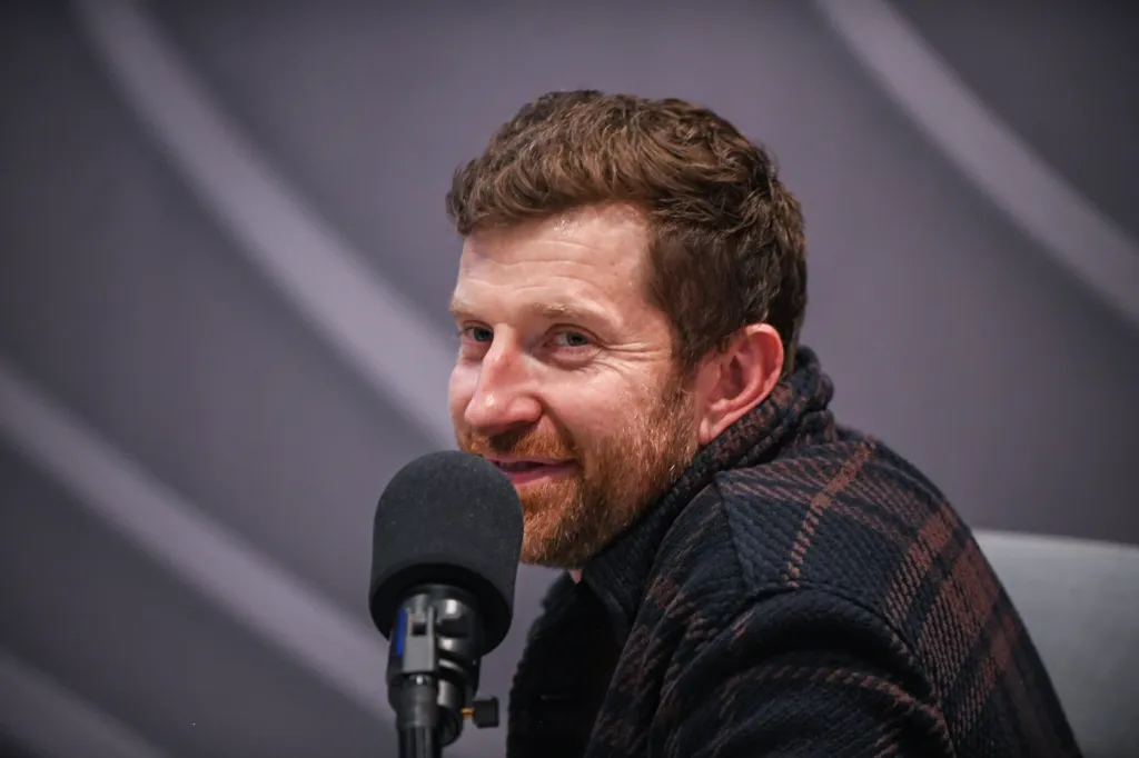 Recording artist Brett Eldredge sits in front of a microphone, wearing a plaid jacket.