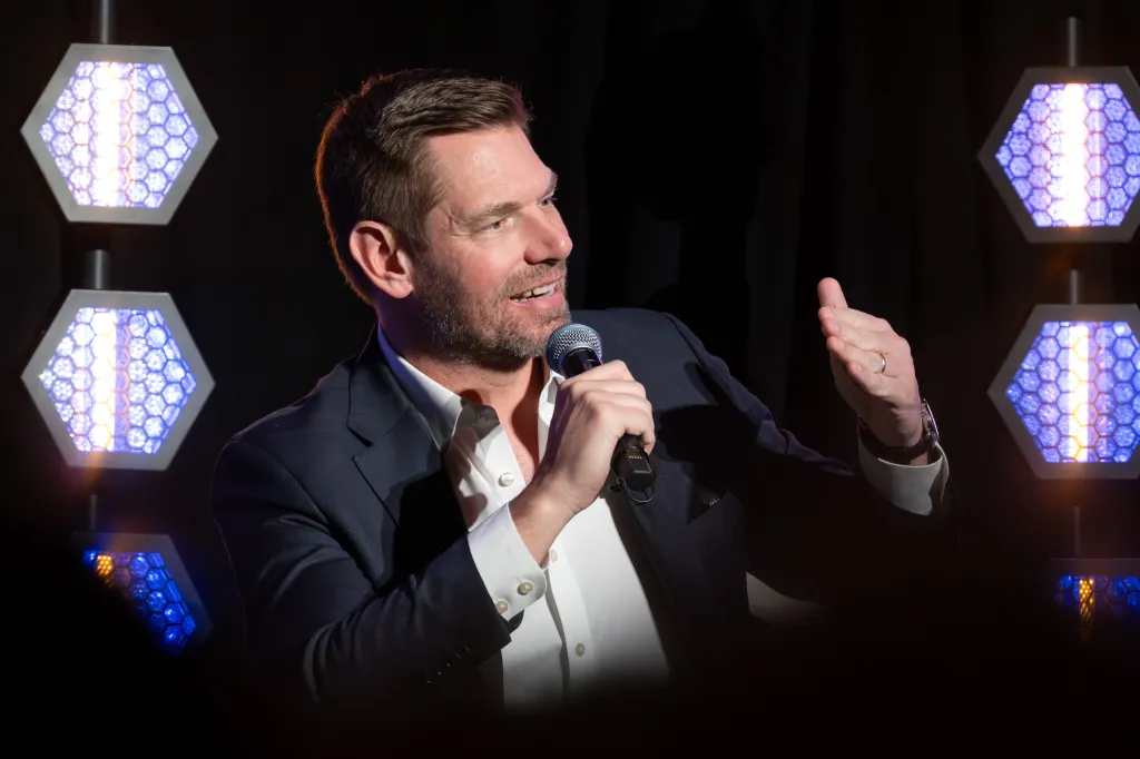 Rep. Eric Swalwell speaks into a microphone while gesturing with his left hand.
