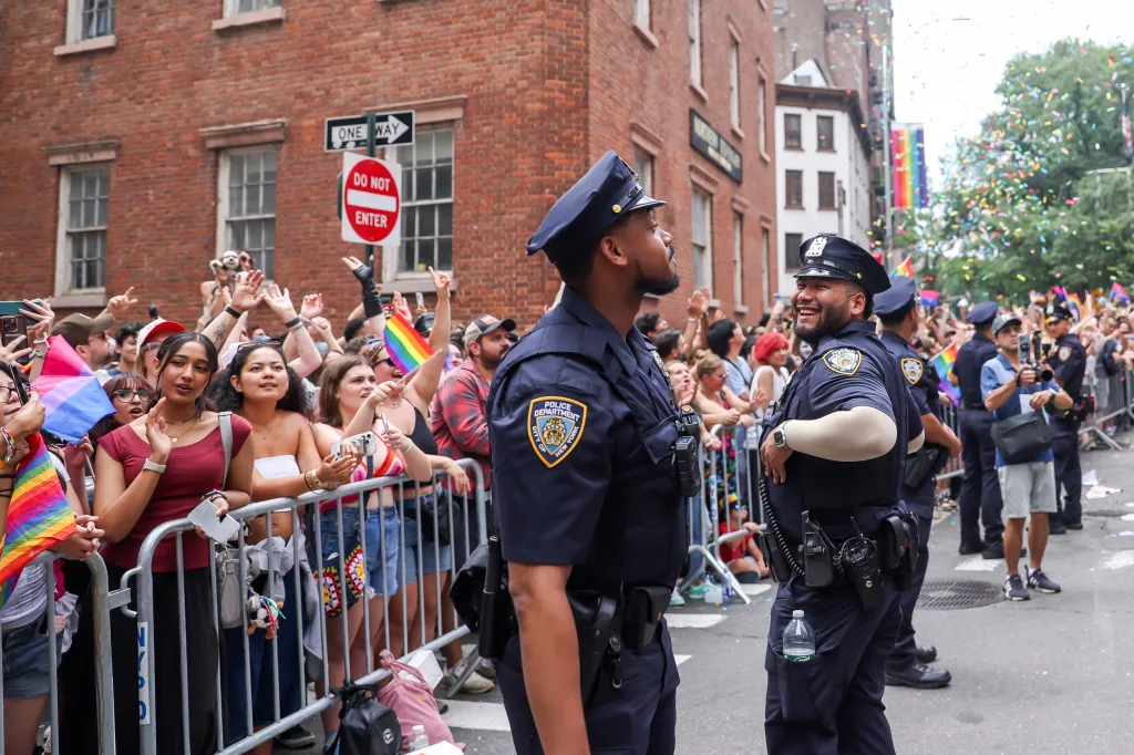 NYC Pride March revelers and two New York Police Department officers stand on a street.