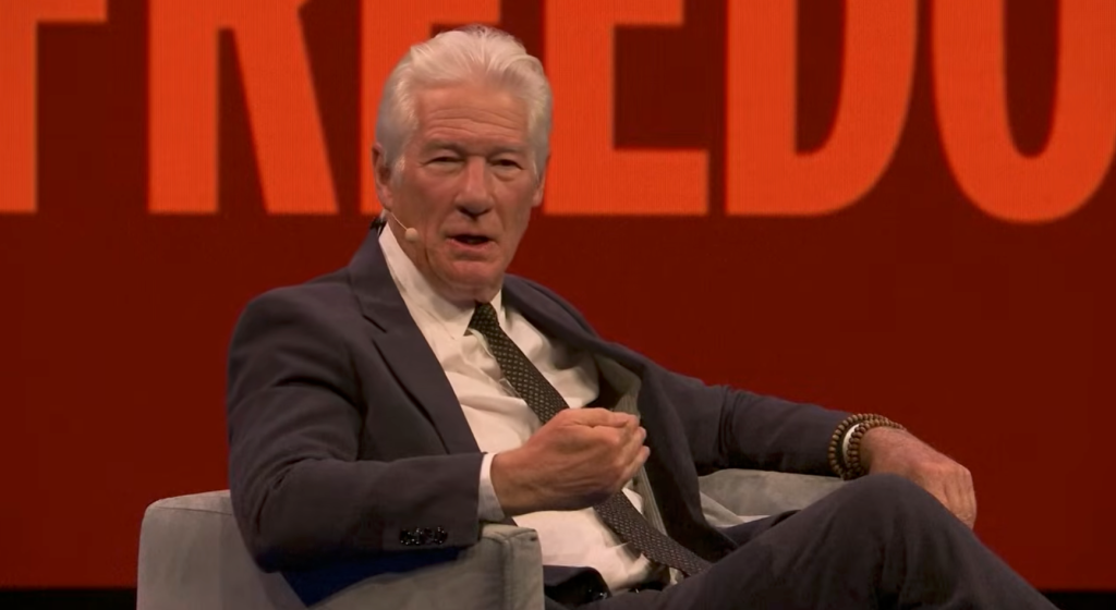 Richard Gere speaking while seated, with a microphone near his mouth.