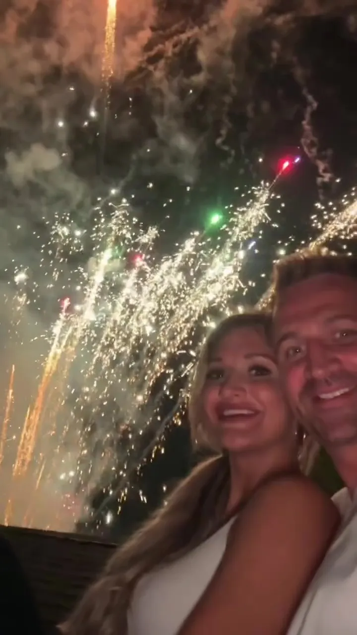 Ryan Lochte and Molly Gillihan smiling with fireworks in the background.