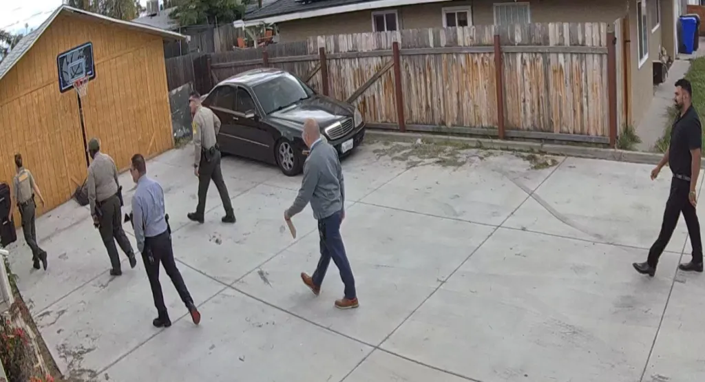 San Bernardino County Sheriff's Department deputies and civilians walk in a fenced backyard.