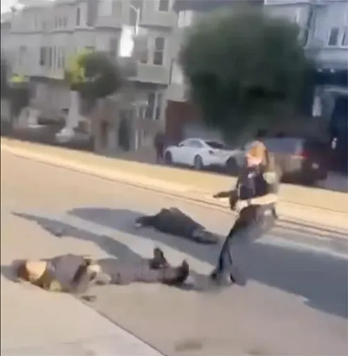 A police officer stands over two people lying on the ground in a street.