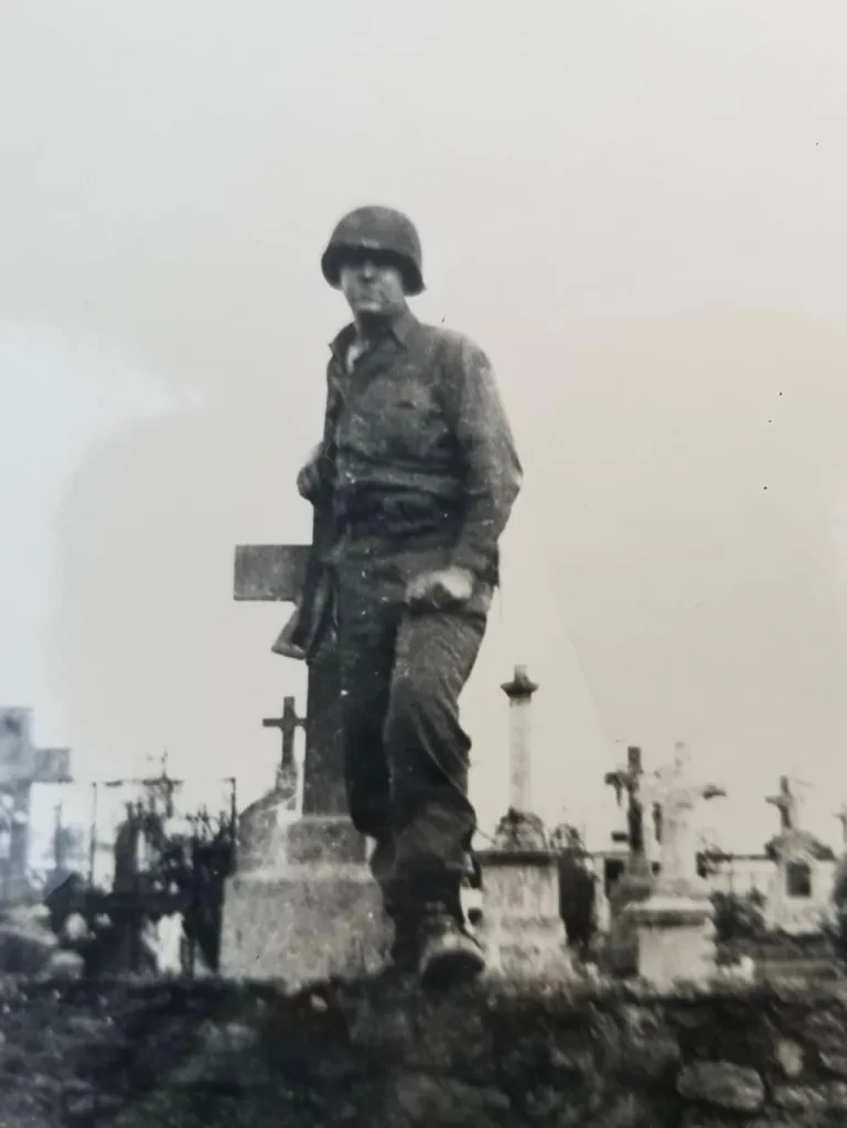 Black and white photo of a soldier in uniform standing among graves.