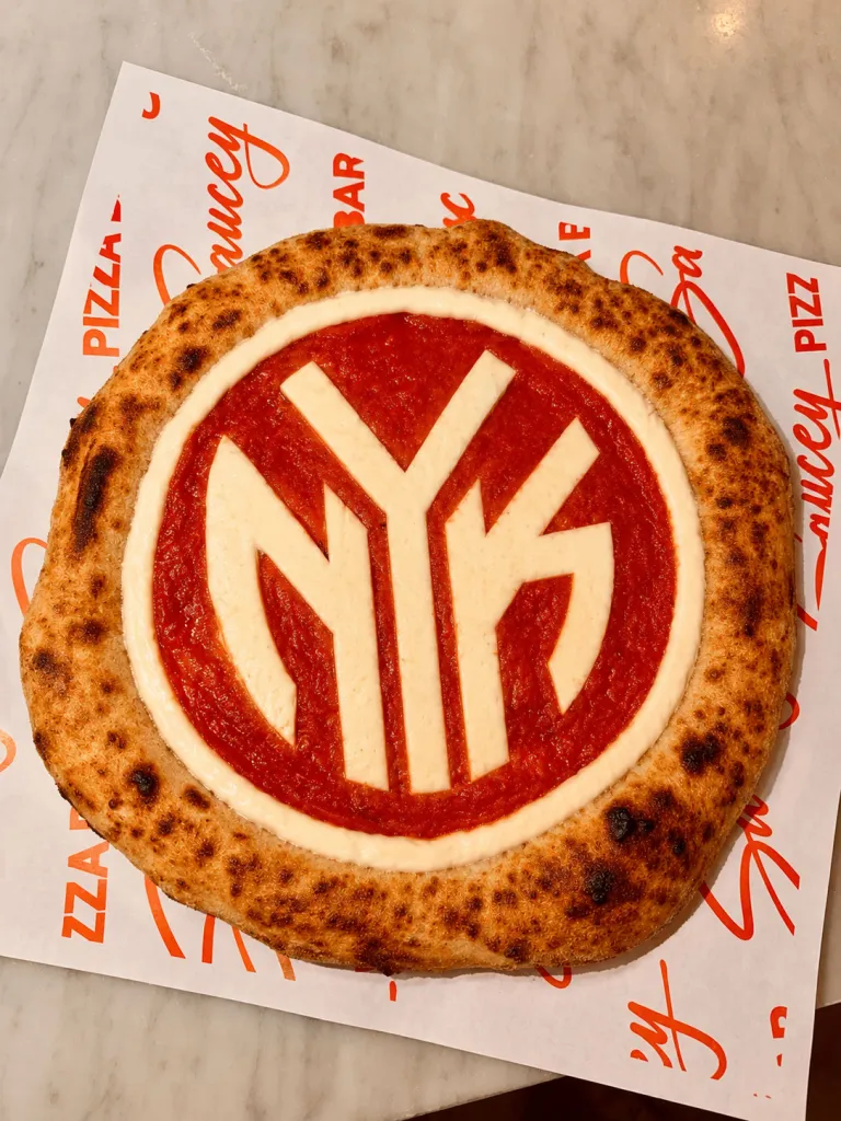Pizza with the NYK logo in cheese and tomato sauce.