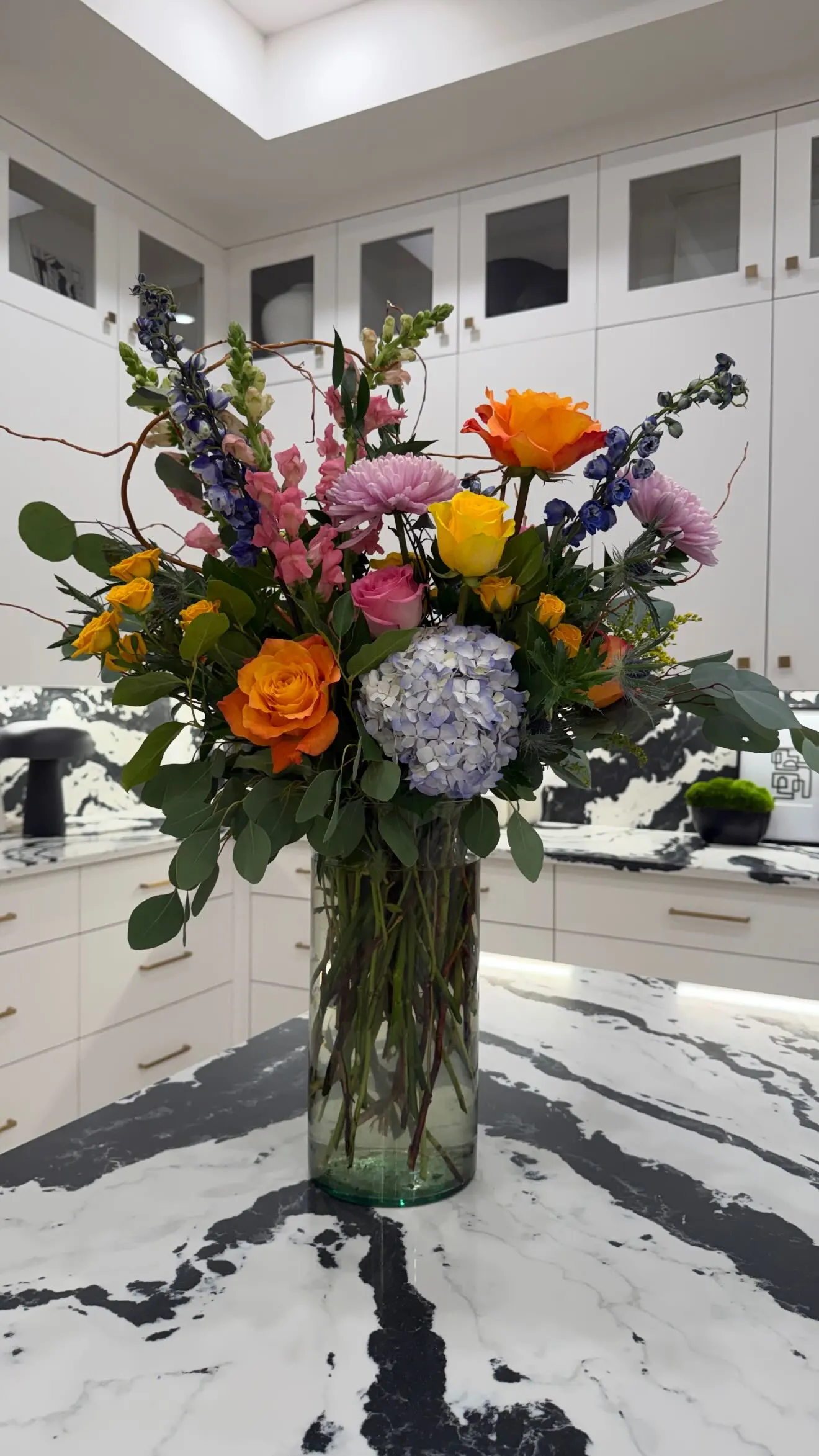 A vibrant bouquet of flowers in a clear vase sits on a black and white marble countertop.