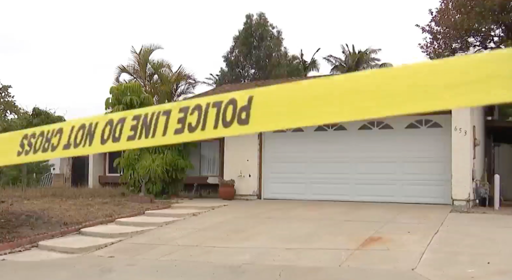 Police tape blocks the front of a house with a garage and driveway.