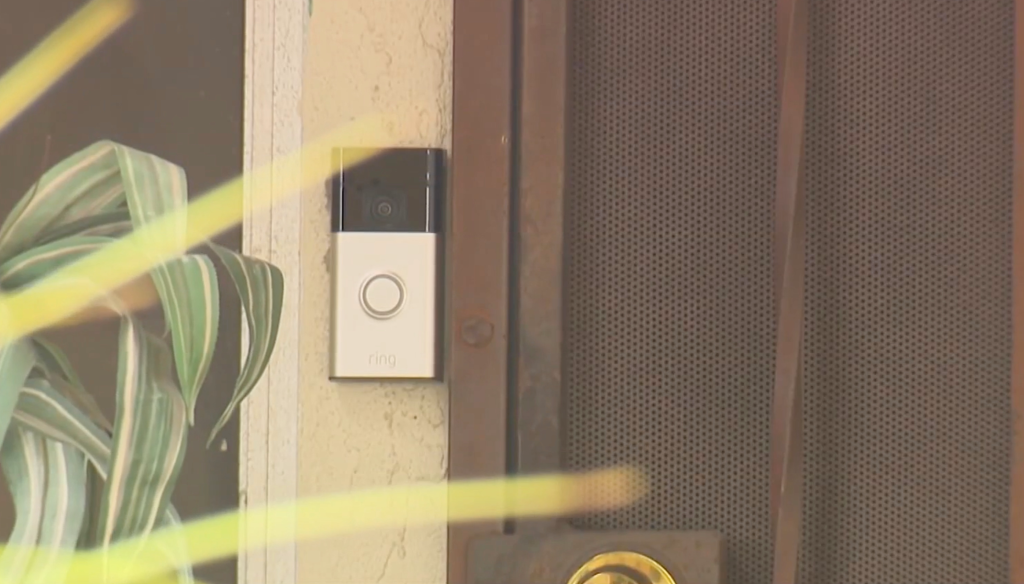 A Ring doorbell on an off-white textured wall next to a brown door with a perforated metal screen.